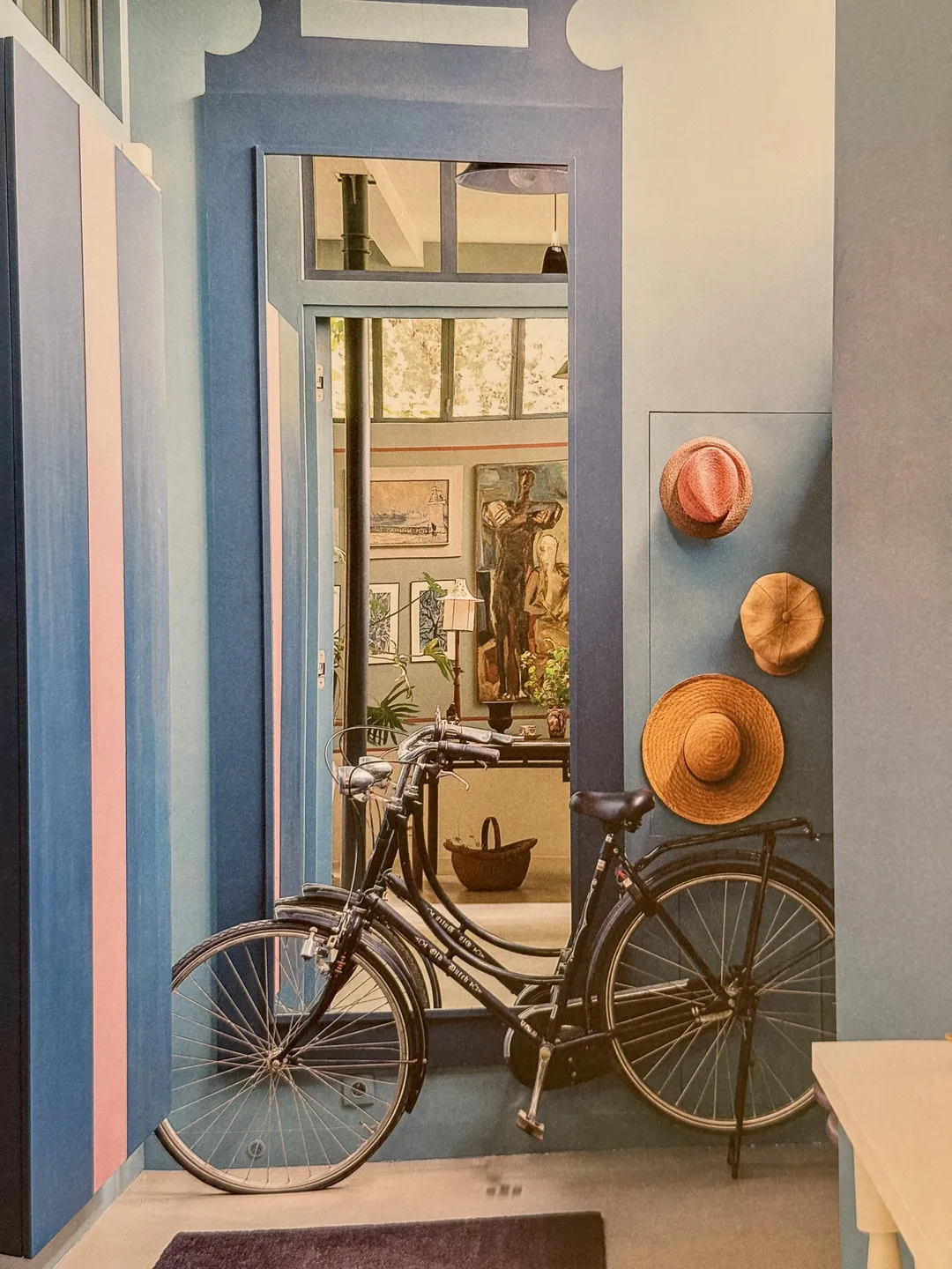Blue painted hallway with a vintage bicycle and straw hats on the wall
