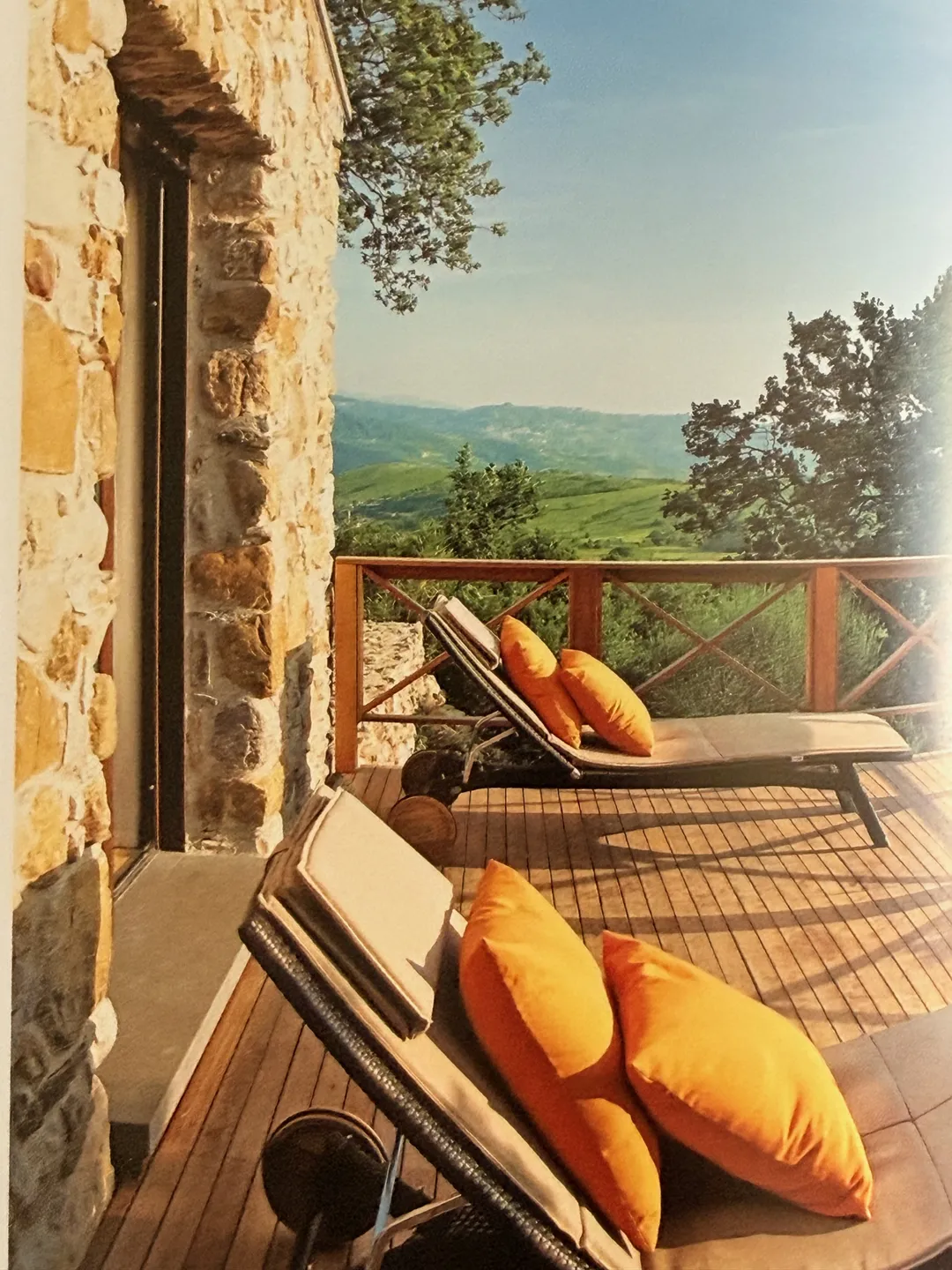 Wooden deck with orange-cushioned loungers overlooking vineyard hills