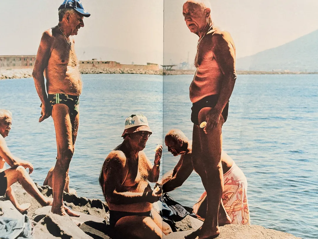 Bronzed older men chatting on the rocks by the Bay of Naples