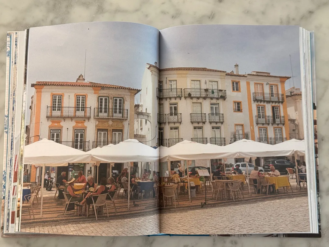 Town square with café umbrellas before pastel buildings with iron balconies
