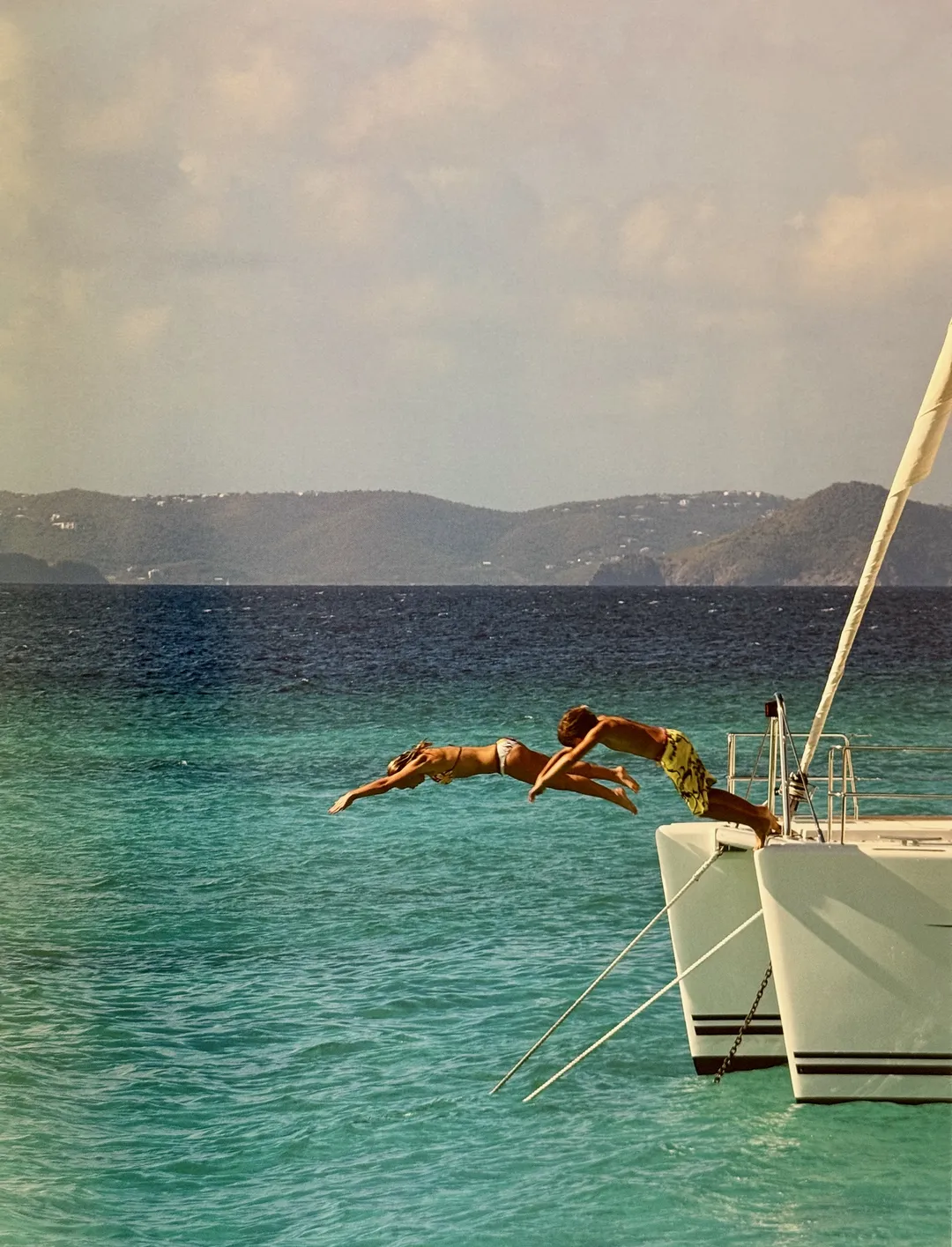 Swimmers diving off a catamaran bow into turquoise water