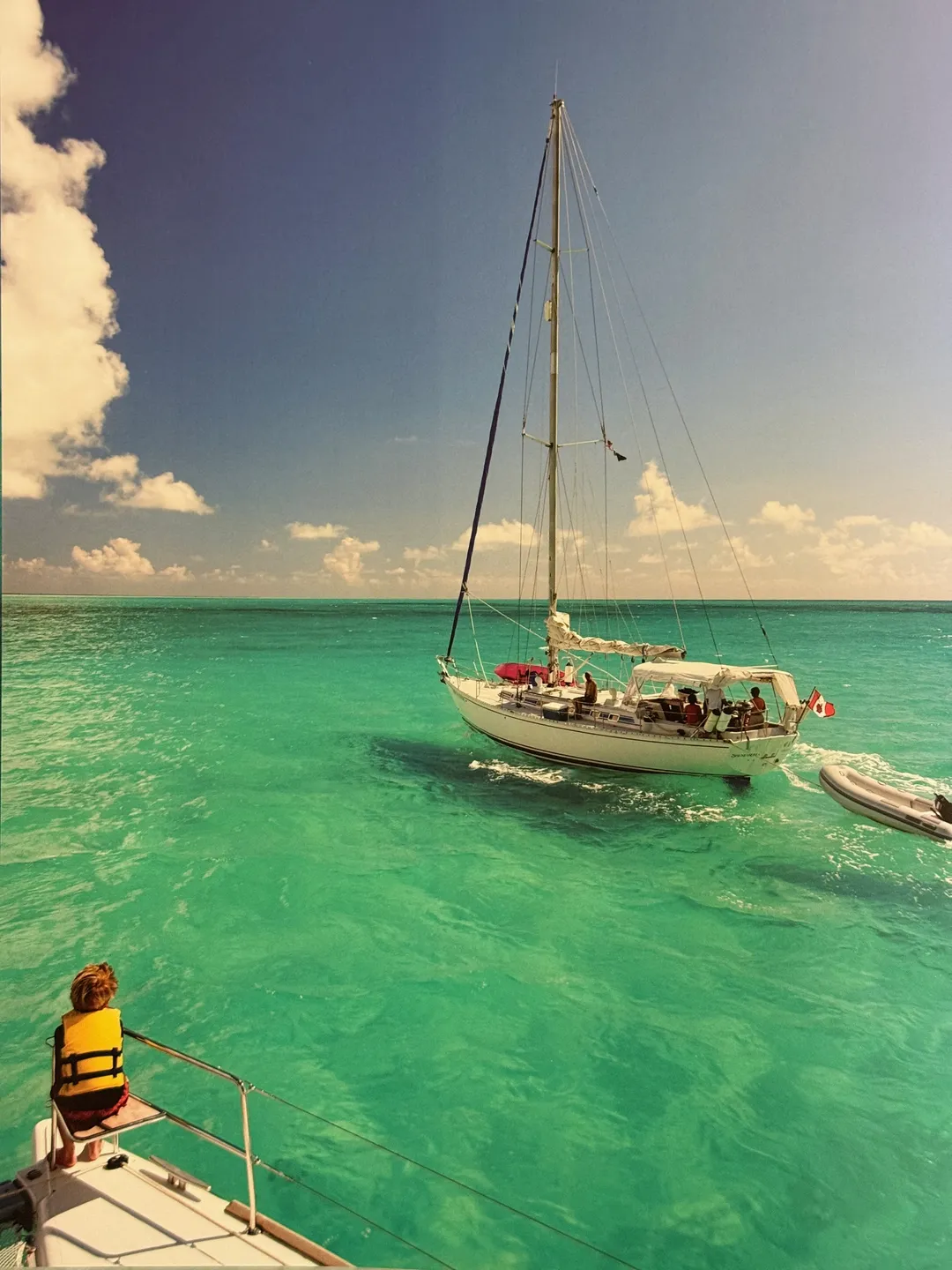 Classic yacht anchored in emerald water, a child in a life jacket on the bow