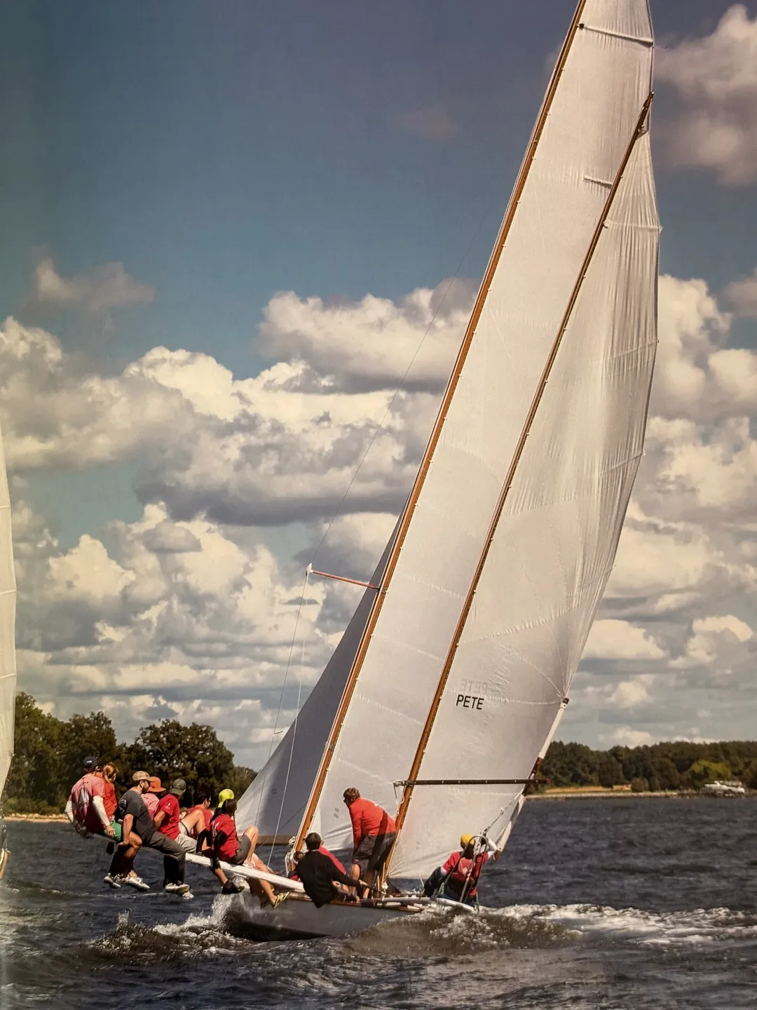 Crew hiking out on a heeling sloop under summer clouds