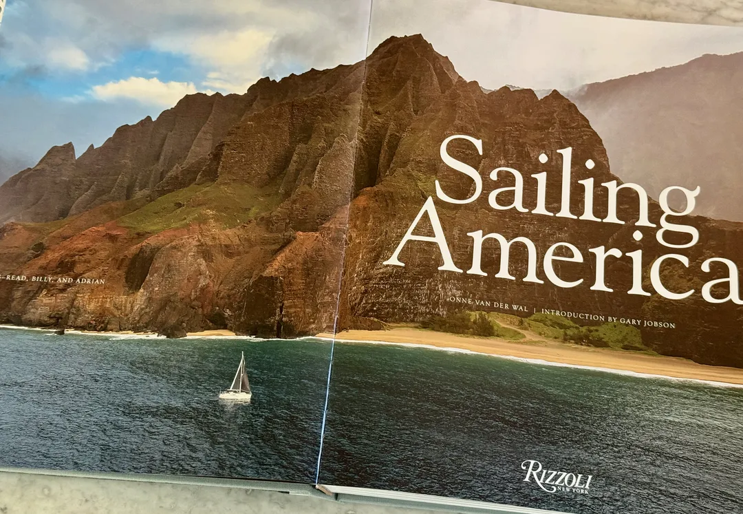 Wraparound jacket: a small sailboat beneath dramatic sea cliffs