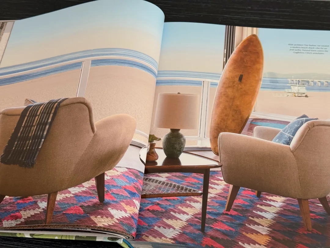 Beach-house sitting room with sculptural armchairs, a surfboard and a kilim rug