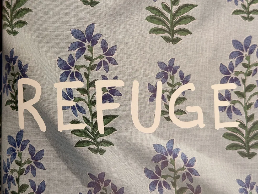 The word REFUGE hand-lettered over a blue floral textile
