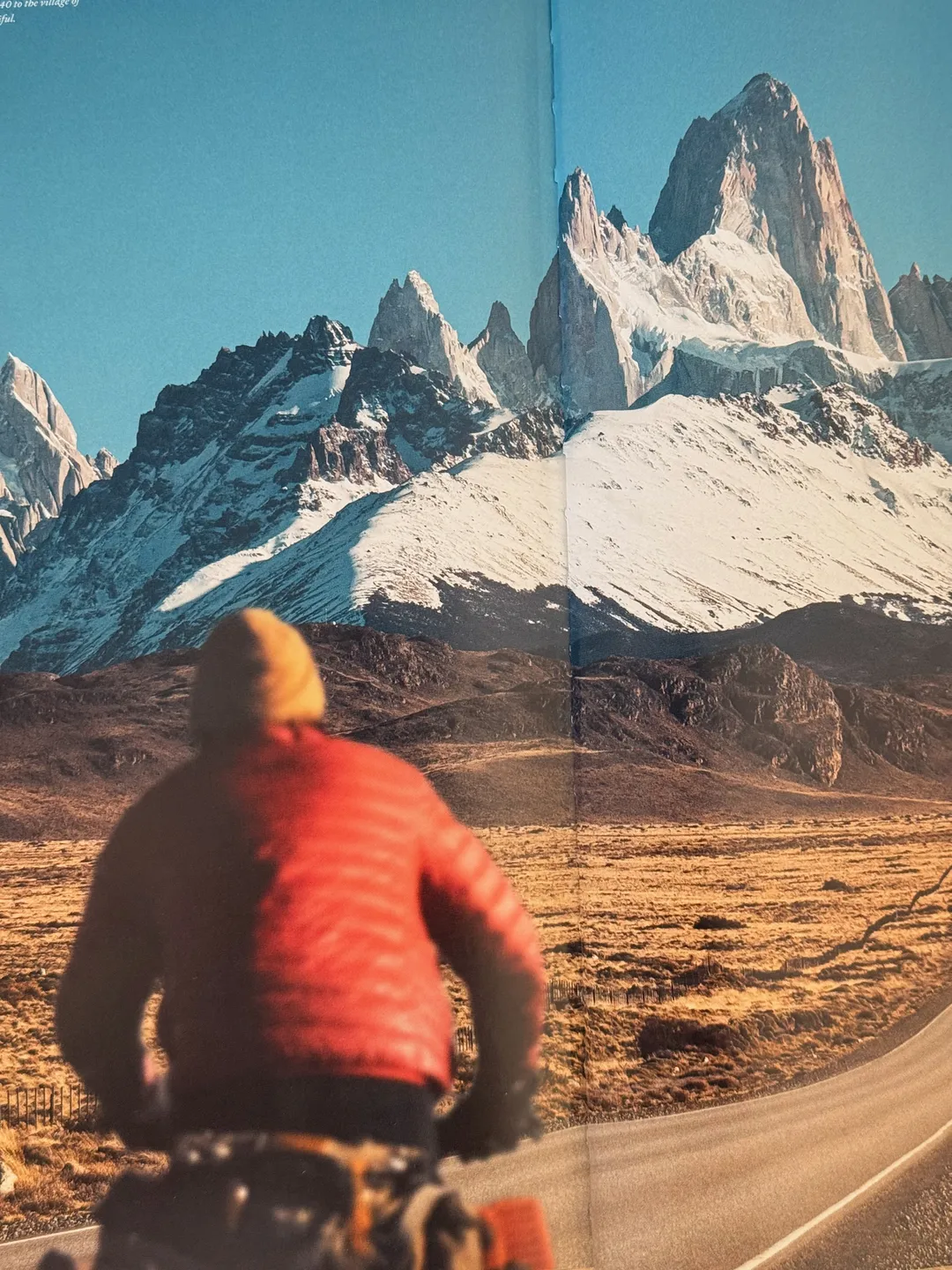 Cyclist in a red jacket riding toward jagged snow-capped peaks in Patagonia